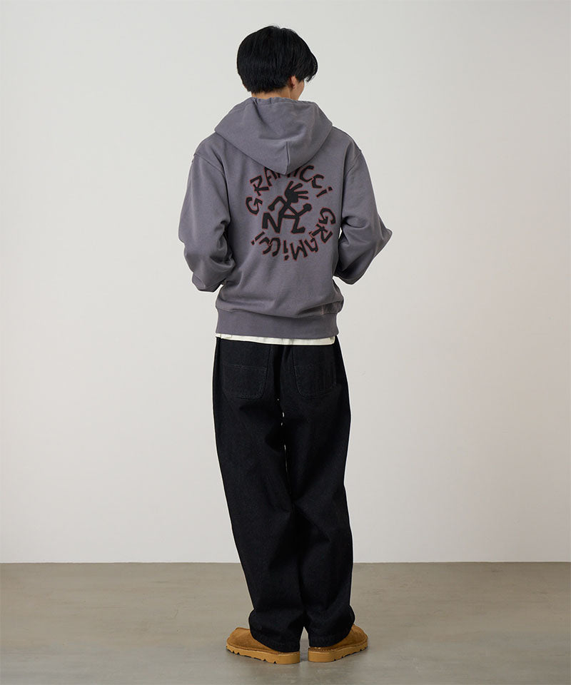 Back view of a model wearing charcoal Gramicci Running Man Zip Hooded Sweatshirt with a running man lsogo and a black pants on a light-tone background.