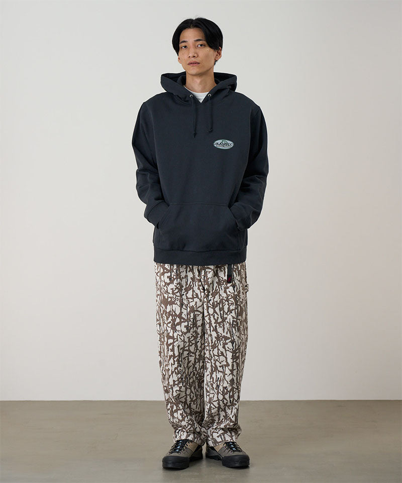 Model wearing a vintage black Gramicci Half Dome Hooded Sweatshirt with a beige and green graphic and camouflage pants on a light tone background.