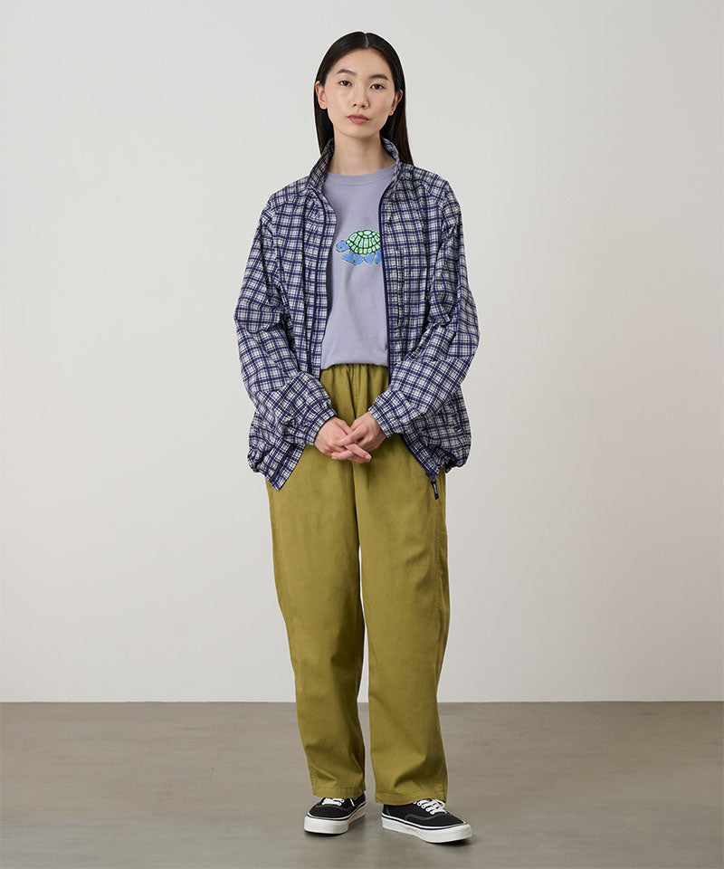 Model wearing grass colored Gramicci Swell Pant and a plaid jacket on a light-tone background.