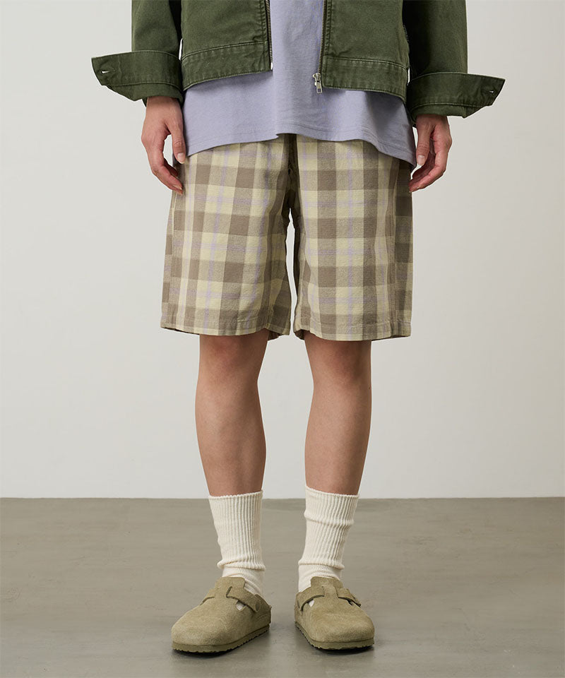 Model wearing shadow plaid colored Gramicci Swell Short Shadow Plaid and a olive jacket on a light-tone background.