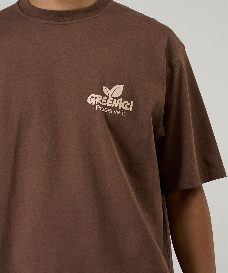 Model wearing a Gramicci brown Greenicci Tee with a graphic against a light tone background.