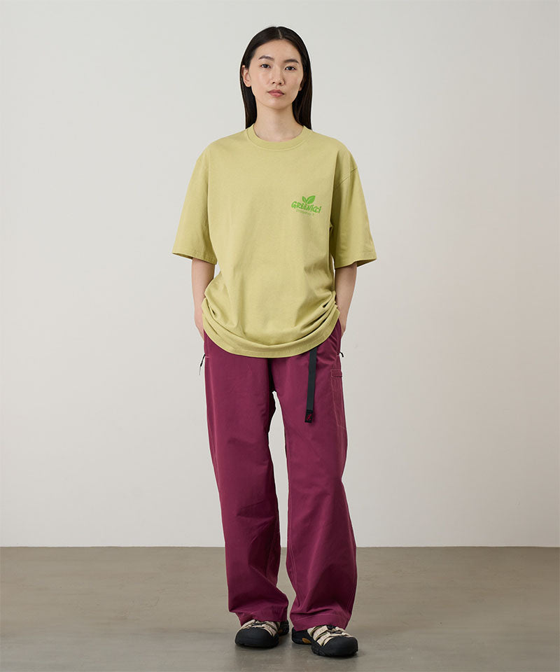 Model wearing a lime Gramicci Greenicci Tee with a graphic and purple pants on a light tone background.