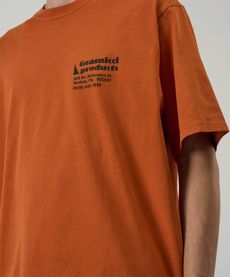 Model wearing a Gramicci orange G-Sail Tee with black graphic against a light-tone background.