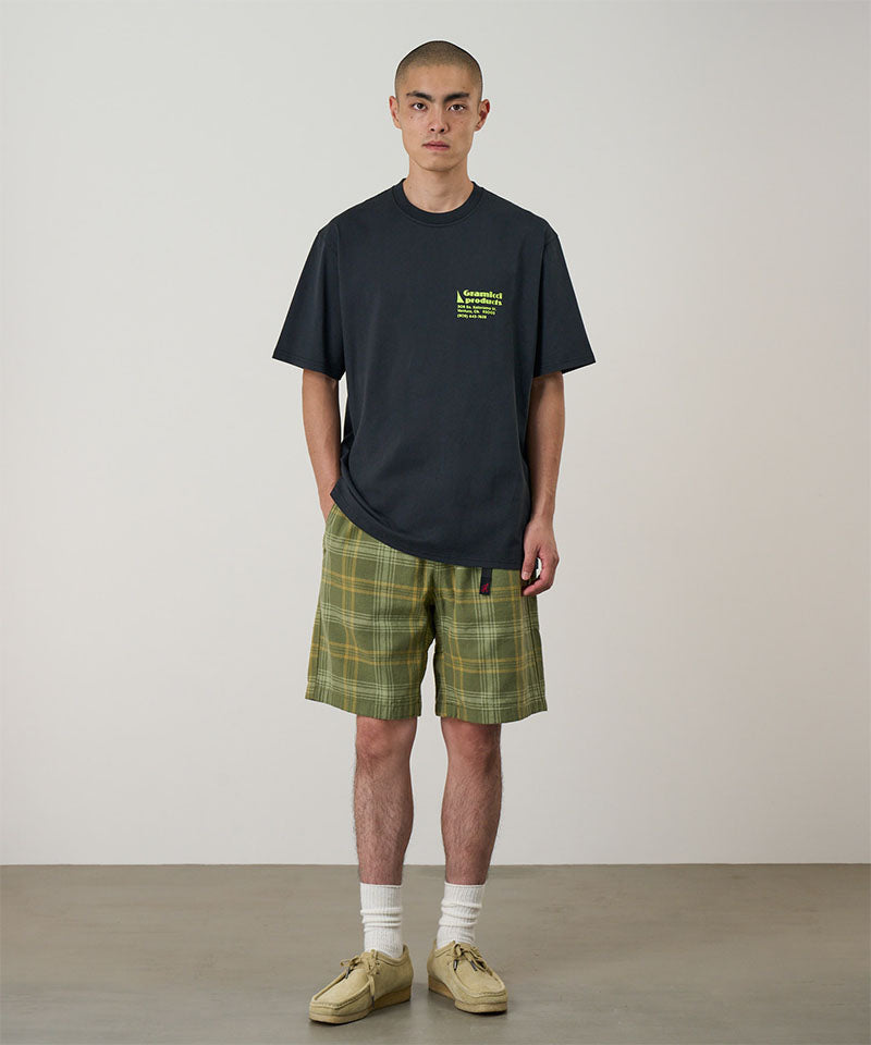 Model wearing a vintage black Gramicci G-Sail Tee with a yellow graphic and green plaid pants on a light-tone background.