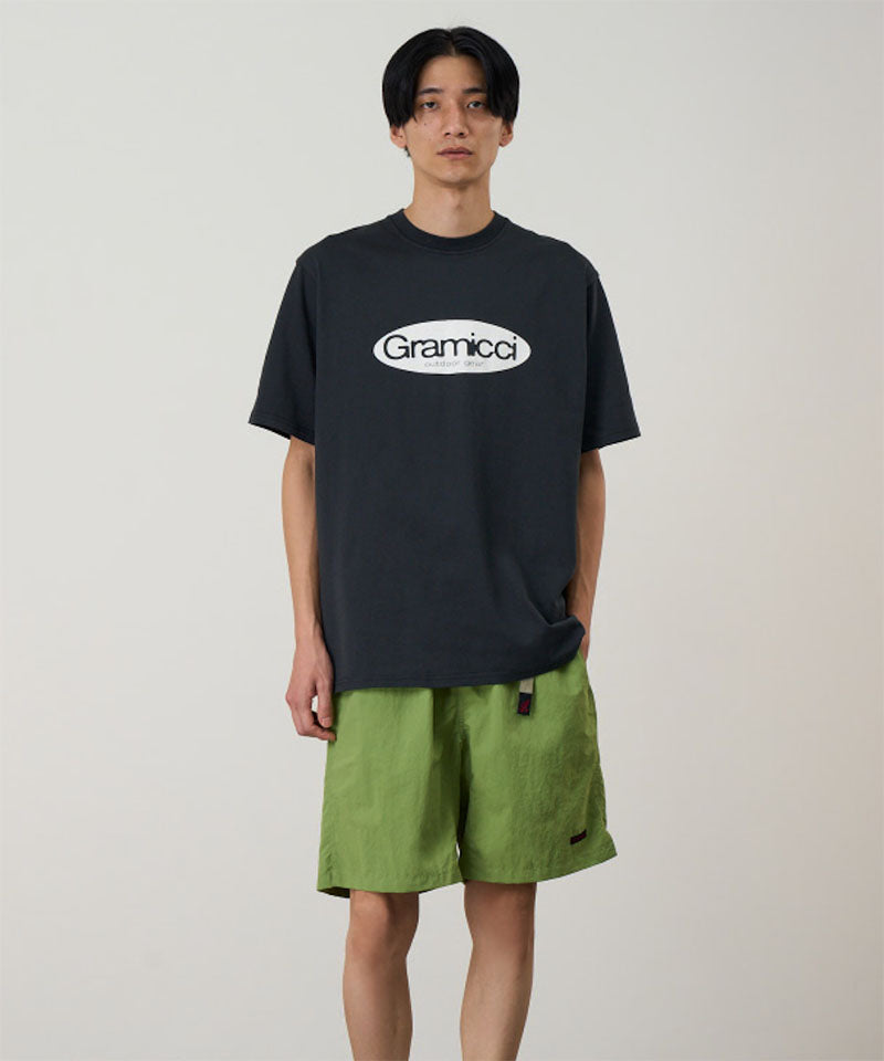 Model wearing a vintage black Gramicci Outdoor Gear Tee with a light beige graphic and green shorts on a light-tone background.