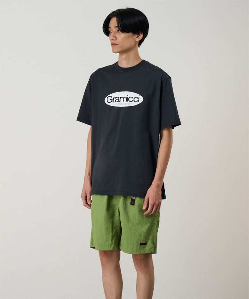 Model wearing a vintage black Gramicci Outdoor Gear Tee with a light beige graphic and green shorts on a light-tone background.