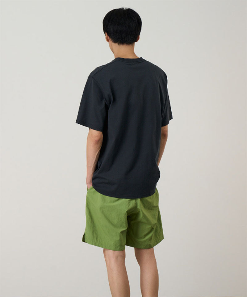 Back view of a model wearing a vintage black Gramicci Outdoor Gear Tee and green shorts on a light-tone background.