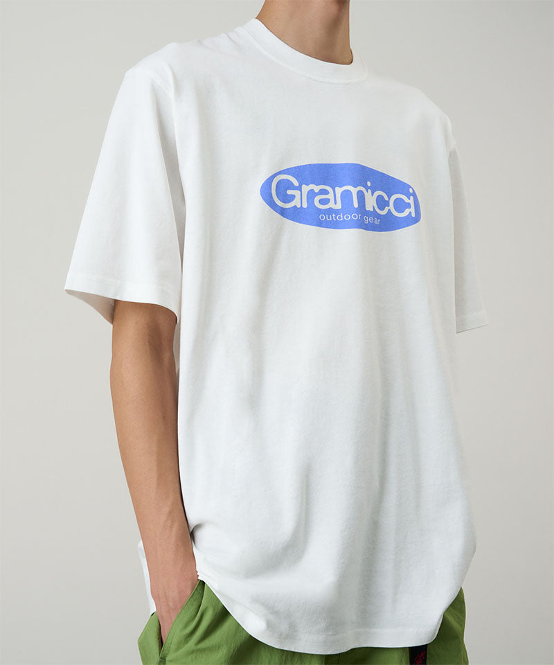 Model wearing a Gramicci white Outdoor Gear Tee with a blue graphic against a light-tone background.