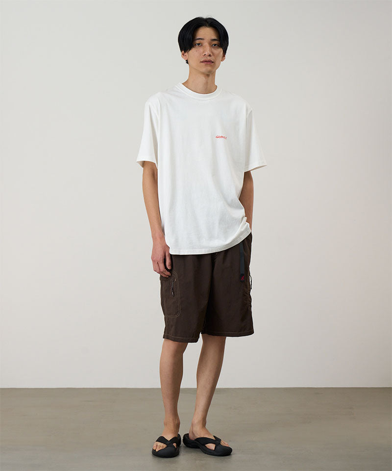Model wearing a white Gramicci Ice Sculpture Tee with a Gramicci graphic and blue shorts on a light tone background.