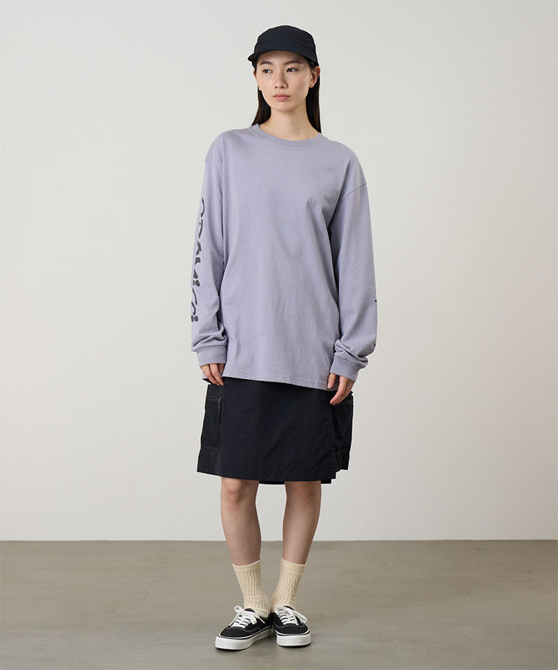 Model wearing a lavender Gramicci Freedom L/S Tee with a black graphic on sleeves and black skort on a light tone background.