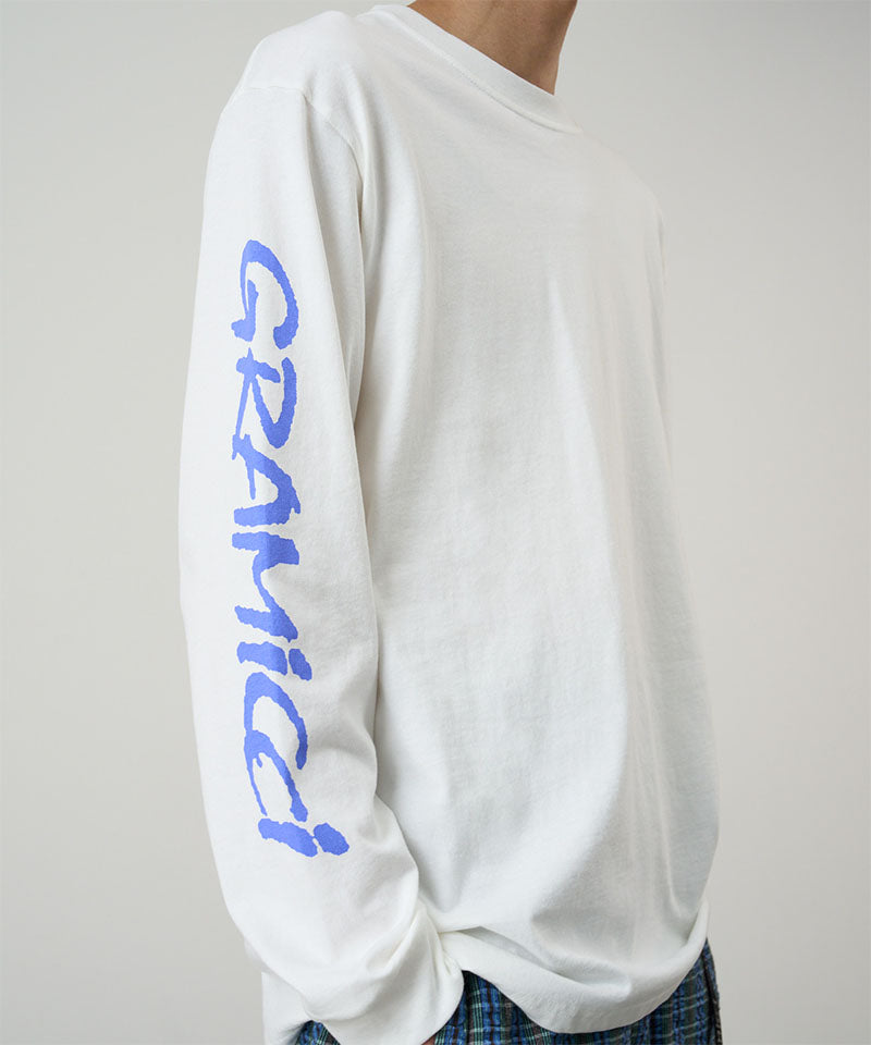 Model wearing a Gramicci white Freedom L/S Tee with blue graphic on sleeves against a light tone background.