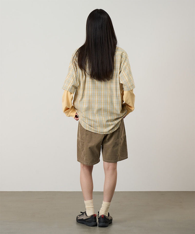 Back view of a model wearing beige Gramicci Women's Corduroy Utility Short and a green plaid shirt on a light-tone background.