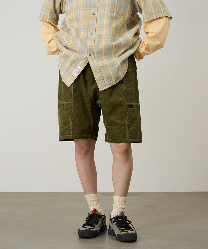 Model wearing olive Gramicci Women's Corduroy Utility Short and a green plaid shirt on a light-tone background.