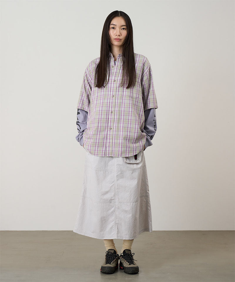 Model wearing a ecru colored Gramicci Nylon Utility Skirt and plaid shirt on a light-tone background.