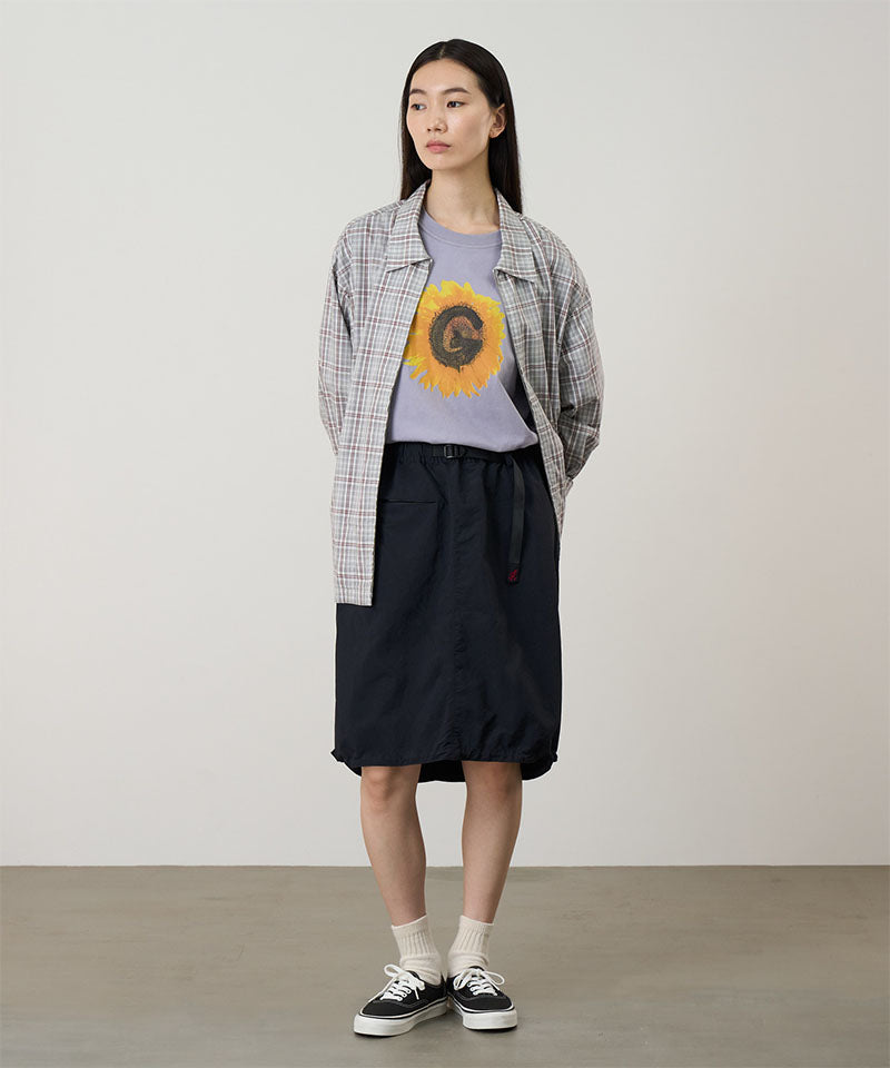 Model wearing a black Gramicci Nylon Packable Midi Skirt and plaid shirt over a sunflower tee on a light-tone background.