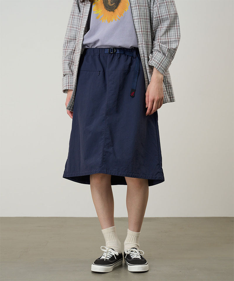 Model wearing a british anavy colored Gramicci Nylon Packable Midi Skirt and plaid shirt over a sunflower tee on a light-tone background.
