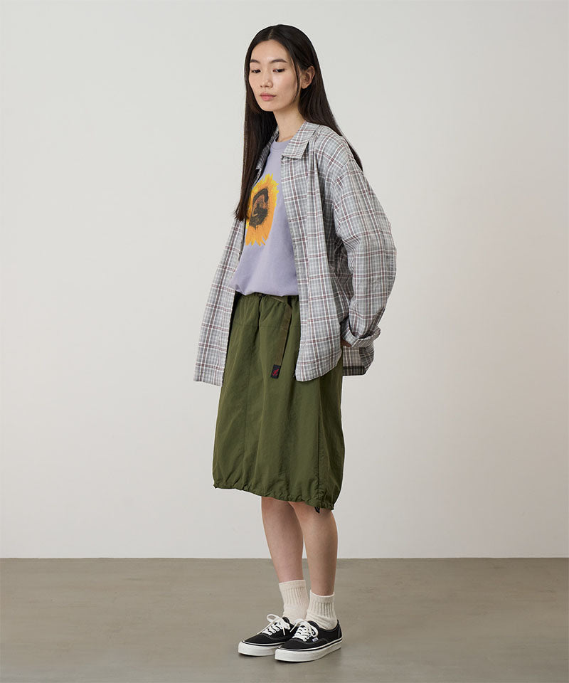 Model wearing an olive colored Gramicci Nylon Packable Midi Skirt and plaid shirt over a sunflower tee on a light-tone background.