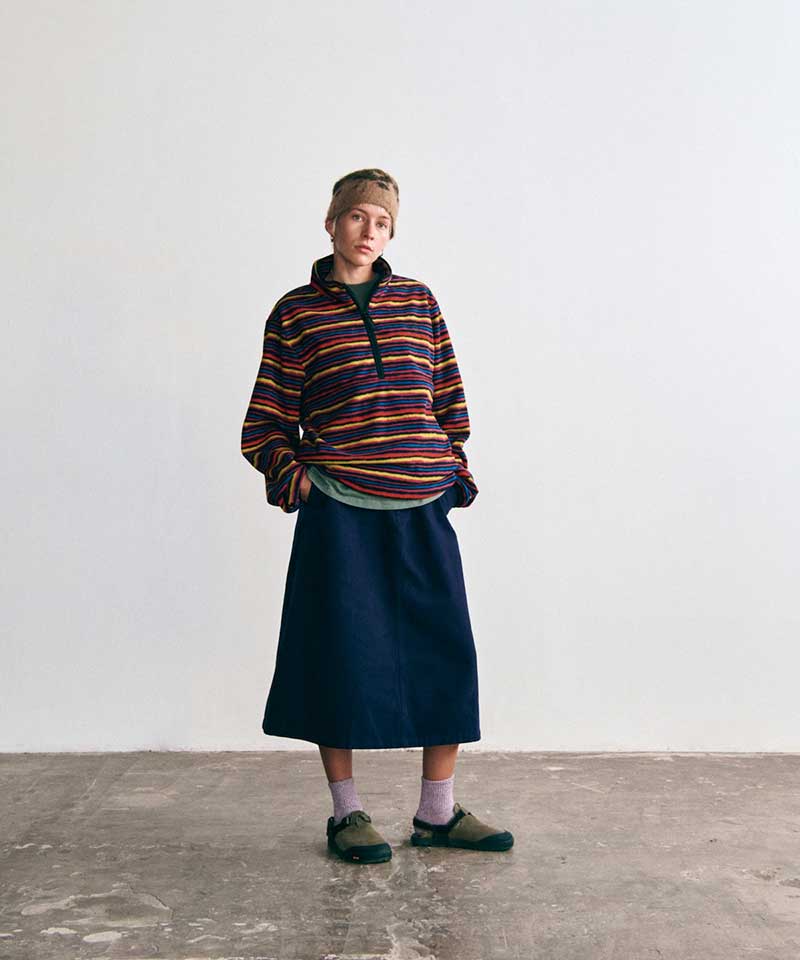 Model wearing a Gramicci multicolored striped fleece pullover, a navy midi skirt, a tan headband, lavender socks, and olive-green outdoor sandals.