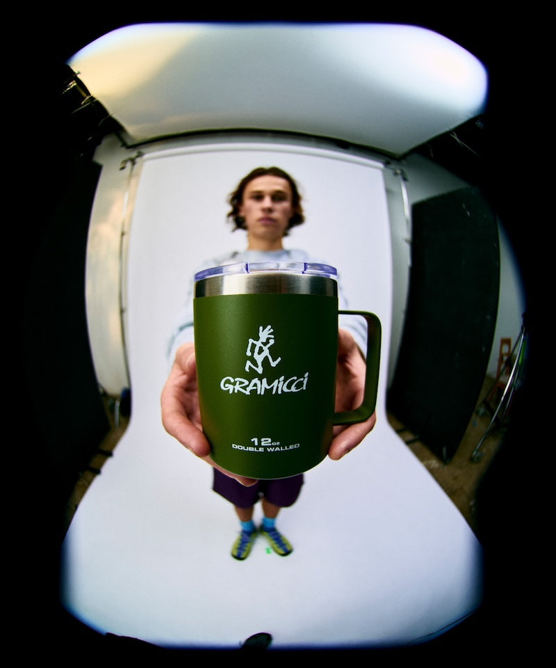 Person holding a green mug with 'Gramicci' branding in front of a white background