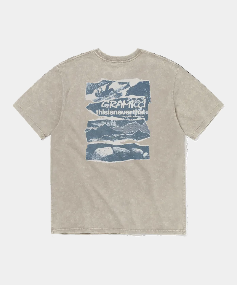 A beige mineral-washed t-shirt with a blue graphic print on the front. The graphic features a mountain scene with the text 'GRAMICCI thisisneverthat'.