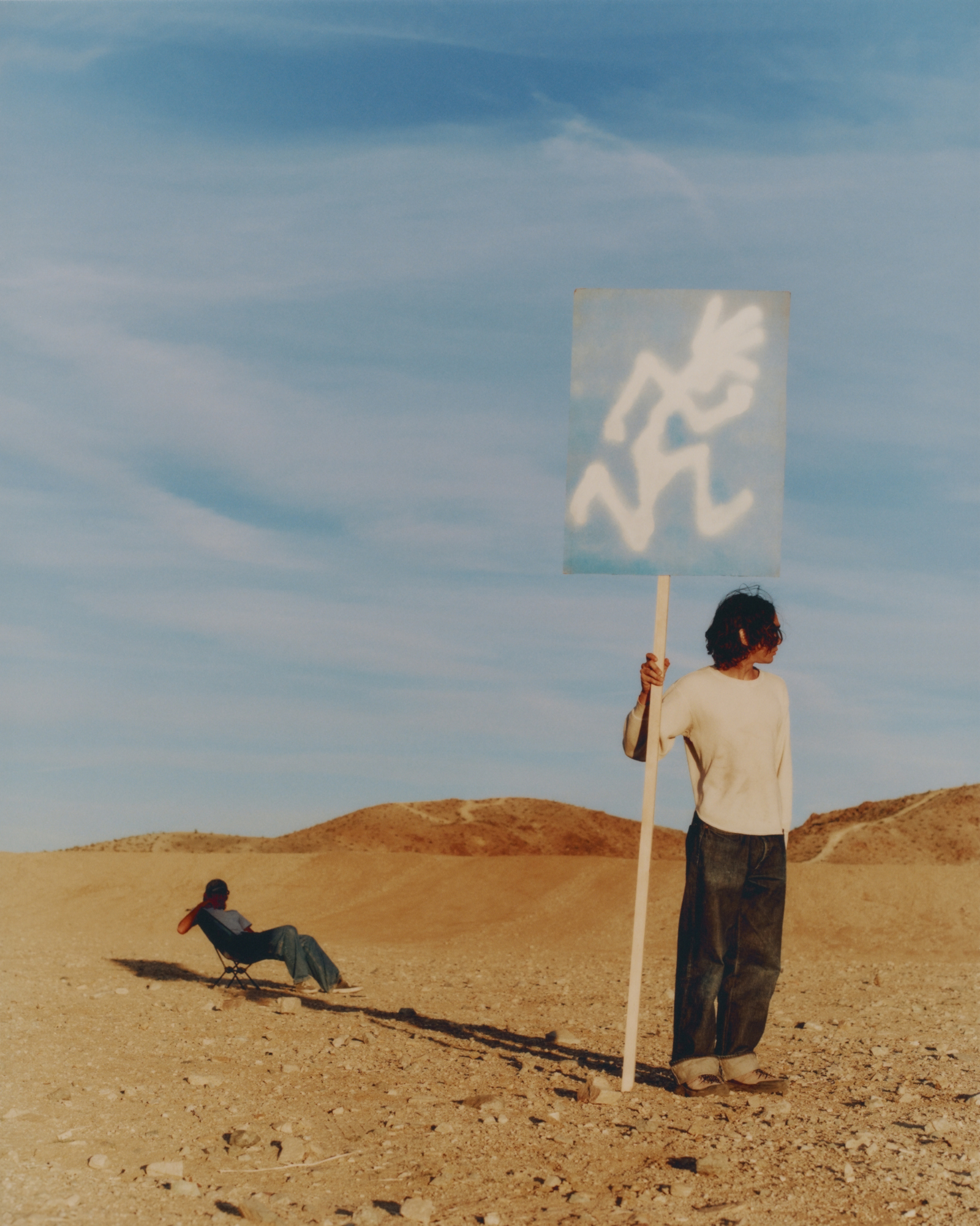 Person holding a sign with a white Gramicci logo in a desert landscape