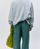 Back view of a model wearinga grey sweatshirt and green pants holding an olive Gramicci Ultra-Light Shopper on a light-tone background.