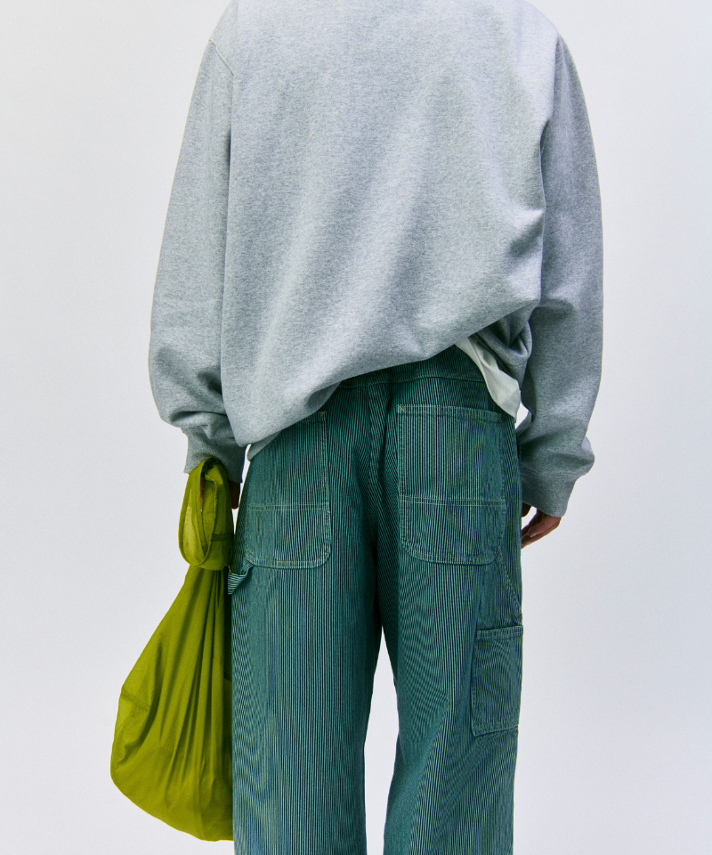 Back view of a model wearinga grey sweatshirt and green pants holding an olive Gramicci Ultra-Light Shopper on a light-tone background.