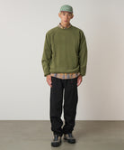 Person wearing a Gramicci green sweatshirt, plaid shirt, black Gramicci Pants, and green cap against a plain background