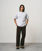 Model wearing a ash heather Gramicci One Point Tee and brown pants on a light-tone background.