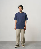 Model wearing a navy Gramicci One Point Tee and beige pants on a light-tone background.