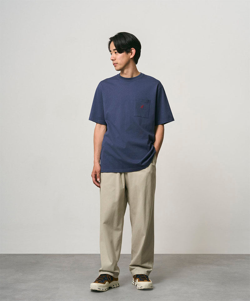 Model wearing a navy Gramicci One Point Tee and beige pants on a light-tone background.