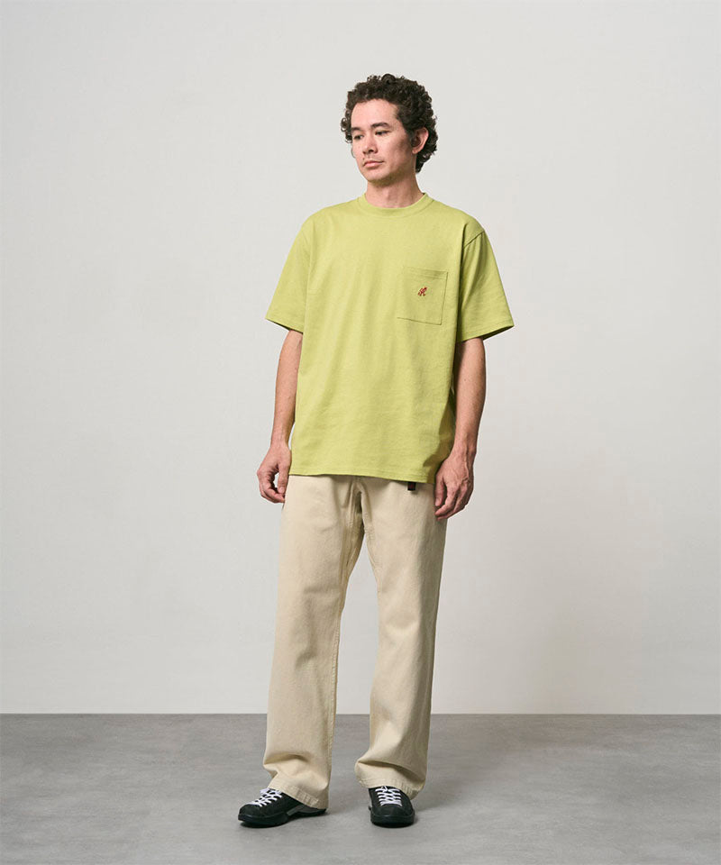 Model wearing a sweet pea colored Gramicci One Point Tee and beige pants on a light-tone background.