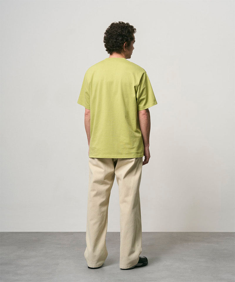 Back view of a model wearing a sweet pea colored Gramicci One Point Tee and beige pants on a light-tone background.