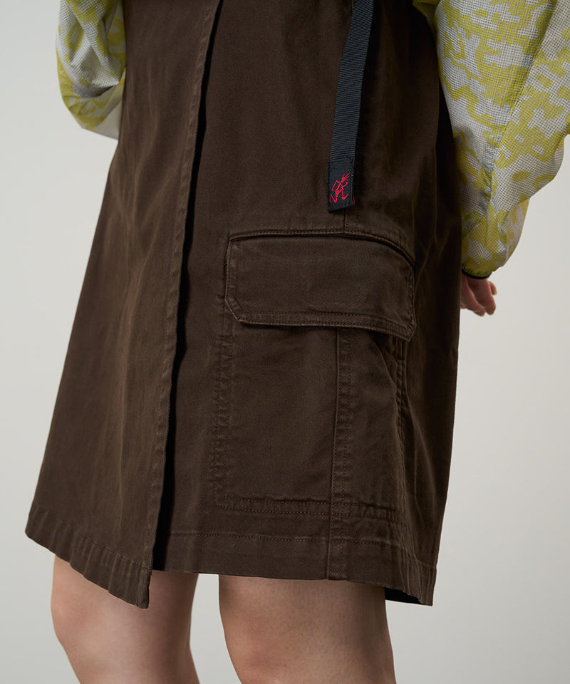 Model wearing a Gramicci dress in the color chocolate and a yellow patterned jacket on a light-tone background.