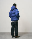 Back view of a model wearing black Nylon Gramicci Pants and a blue jacket on a light-tone background.