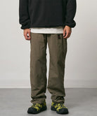 Burnt olive colored Nylon Gramicci Pants with a belt against a light-tone background.