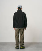 Back view of a model wearing burnt olive colored Nylon Gramicci Pants and a black jacket on a light-tone background.