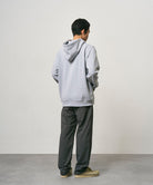 Back view of a model wearing carbon colored  Nylon Gramicci Pants and a grey hoodie on a light-tone background.