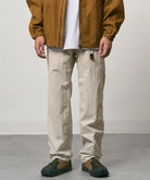 Model wearing stone colored Nylon Gramicci Pants and a brown jacket on a light-tone background.
