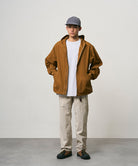 Model wearing stone colored Nylon Gramicci Pants and a brown jacket on a light-tone background.
