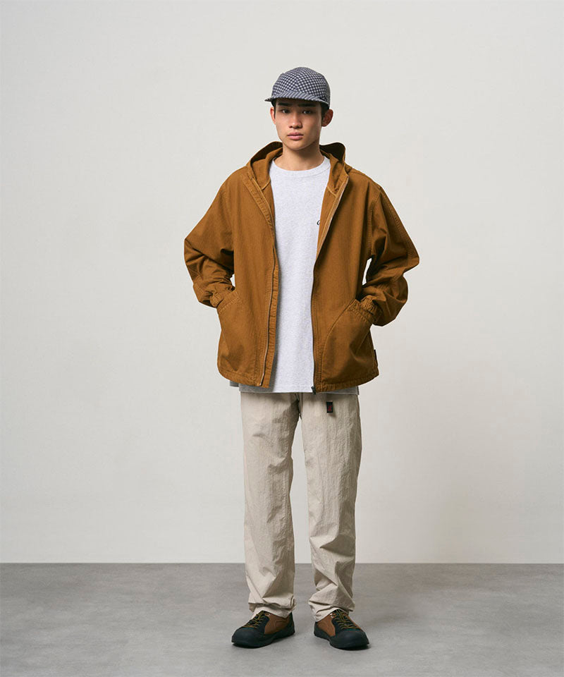 Model wearing stone colored Nylon Gramicci Pants and a brown jacket on a light-tone background.