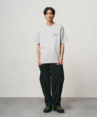 Model wearing a mist colored Gramicci Bass Tee and black pants on a light-tone background.