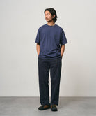 Model wearing a navy Gramicci Bass Tee and black pants on a light-tone background.