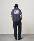 Model wearing a navy Gramicci Bass Tee and black pants on a light-tone background.