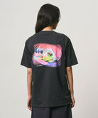 Back view of a model wearing a Gramicci vintage black Bass Tee with a graphic against a light-tone background.