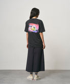 Back view of a model wearing a vintage black Gramicci Bass Tee with a graphic and black skirt on a light-tone background.