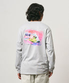 Back view of a model wearing a Gramicci mist colored Bass Long-Sleeve Tee with a graphic against a light-tone background.