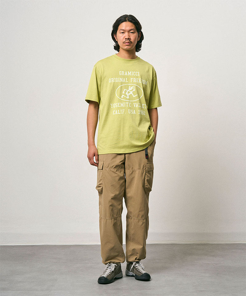 Model wearing a sweet pea colored Gramicci Yosemite Valley Tee with a graphic and beige pants on a light-tone background.