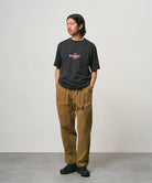 Model wearing a vintage black Gramicci Ladybug Tee with colorful graphic and brown pants on a light-tone background.