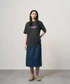 Model wearing a vintage black Gramicci Ladybug Tee with colorful graphic and blue skirt on a light-tone background.